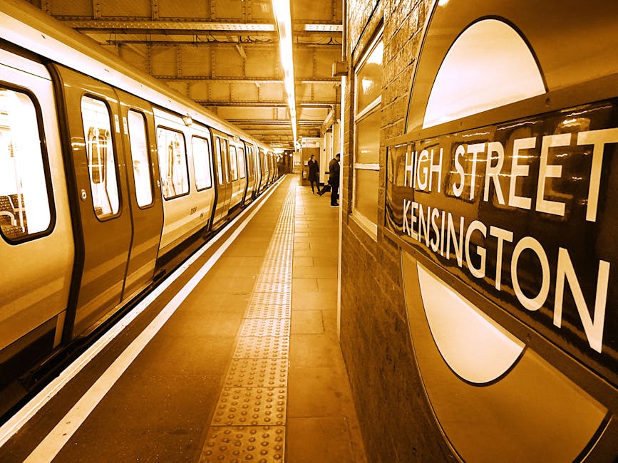 The image shows a well-lit underground station platform at Kensington High Street, W8, with a train parked along the edge. The platform surface appears clean and smooth, made of polished tiles with ta